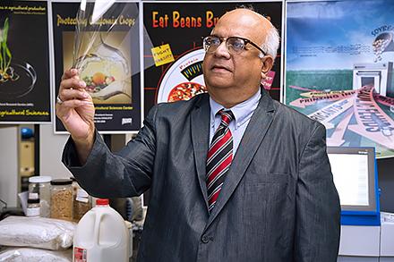 A man in a suit jacket, tie, and glasses holds up and looks at a clear rectangular sheet