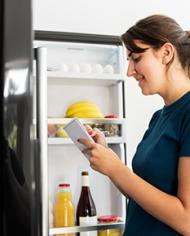 Woman standing in front of an open refrigerator while making a list.